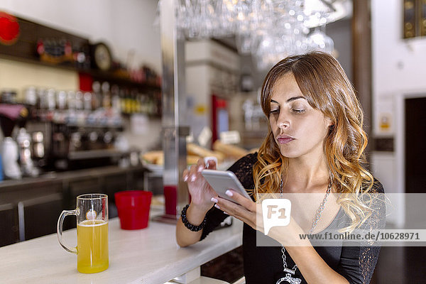 Portrait of serious looking young woman using smartphone in a pub