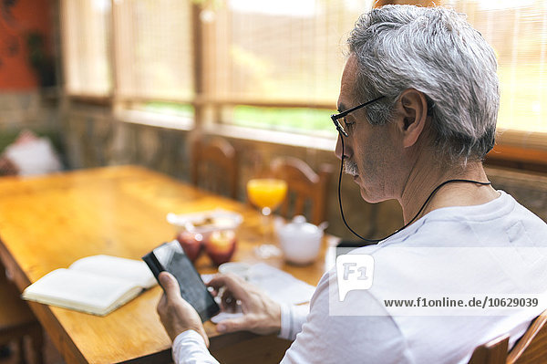 Mann sitzt am Frühstückstisch mit dem Smartphone