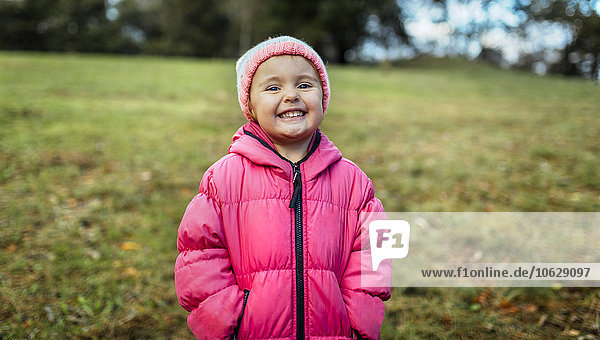 Porträt des lächelnden Mädchens mit Mütze und rosa Jacke im Herbst