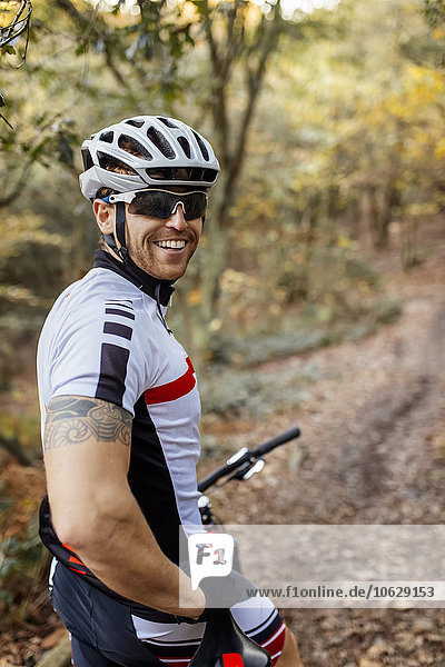 Portrait des lächelnden Mountainbikers mit Fahrradhelm und Sonnenbrille im Wald