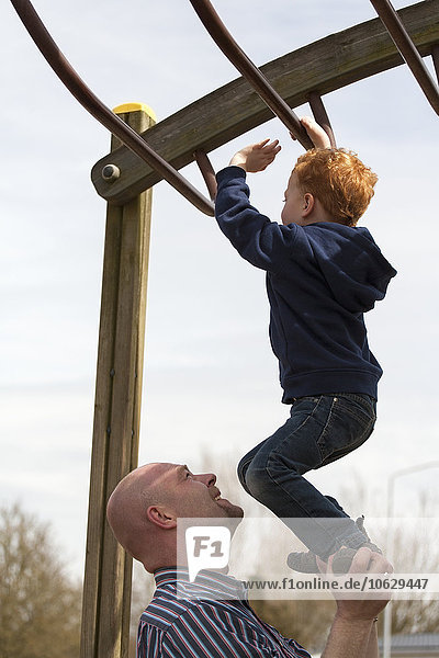 Vater hilft dem Sohn auf dem Spielplatz beim Klettern in der Kletterhalle.