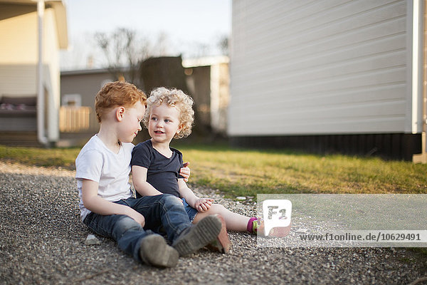 Kleines Mädchen und Junge sitzen auf Schotterpiste