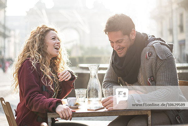 Italy  Milan  laughing couple sitting at sidewalk cafe having fun