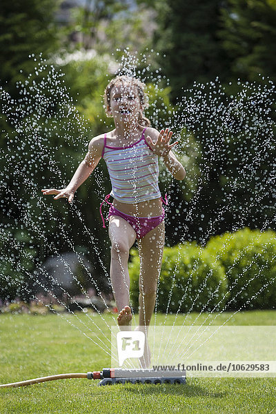 Mädchen springt über Sprinkler im Garten