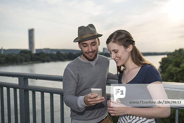 Deutschland  Bonn  junges Paar auf der Rheinbrücke mit Blick auf das Smartphone