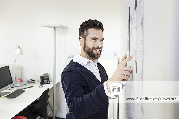 Man in office pointing at wall with papers