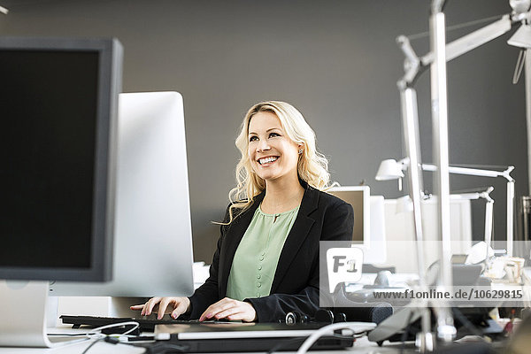 Lächelnde blonde Frau bei der Arbeit am Schreibtisch im Büro