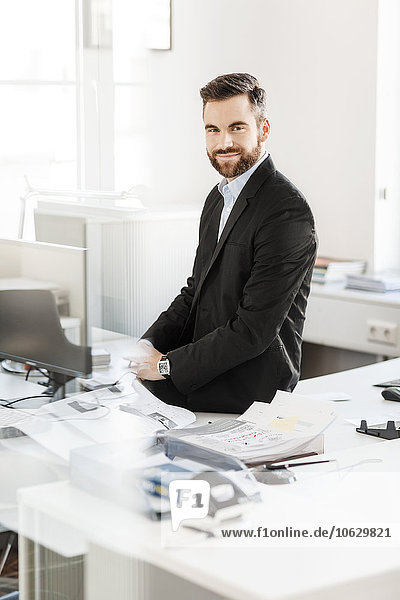 Lächelnder Geschäftsmann auf dem Schreibtisch im Büro sitzend