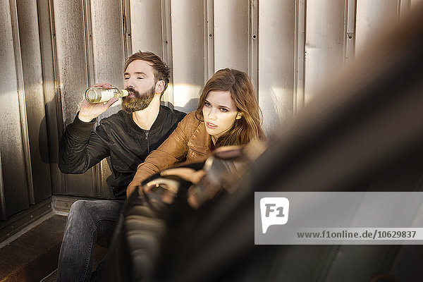 Couple with beer bottle sitting in a garage