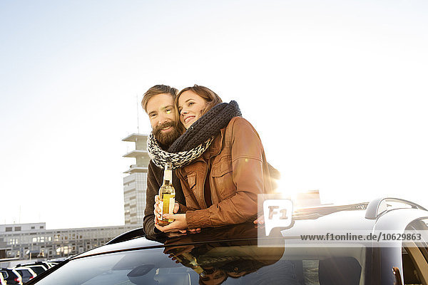 Glückliches Paar schaut durch das Schiebedach eines Autos  das sich einen Schal teilt.