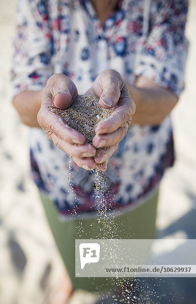Hände einer älteren Frau  die Sand am Strand hält.