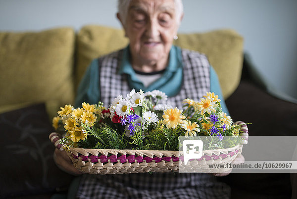 Seniorenfrau zeigt einen mit Kunstblumen geschmückten Korb