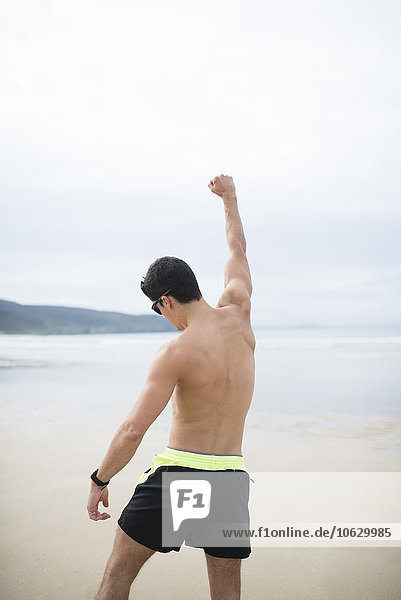 Spanien  Galizien  Ferrol  sportlicher Mann ohne Hemd am Strand mit erhobenem Arm