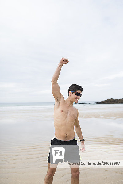 Spanien  Galizien  Ferrol  sportlicher Mann ohne Hemd am Strand mit erhobenem Arm