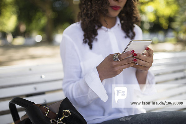 Junge Frau sitzt auf der Parkbank mit ihrem Smartphone  Nahaufnahme
