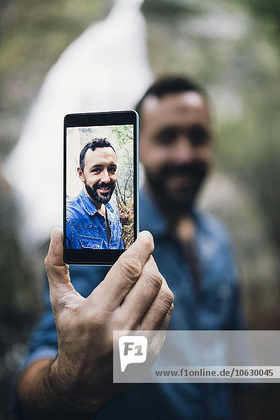 Bärtiger Mann zeigt Selfie auf dem Display seines Smartphones