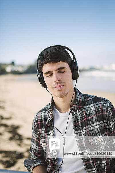 Spain  La Coruna  portrait of young man with headphones on the beach