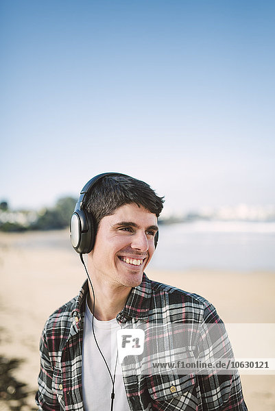 Spain  La Coruna  portrait of smiling man with headphones on the beach