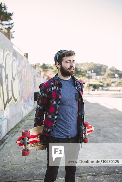 Spain  La Coruna  portrait of hipster with his longboard