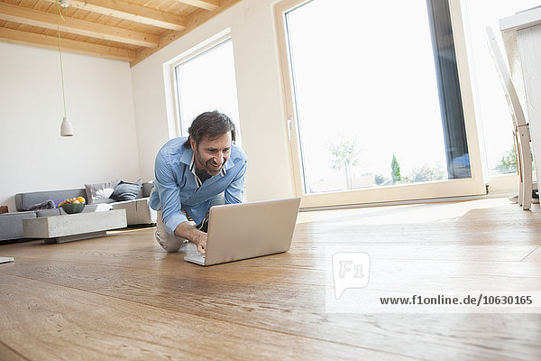 Erwachsener Mann zu Hause mit Laptop auf dem Boden