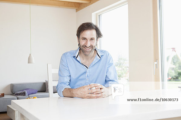 Mature man drinking coffee at table at home looking pleased