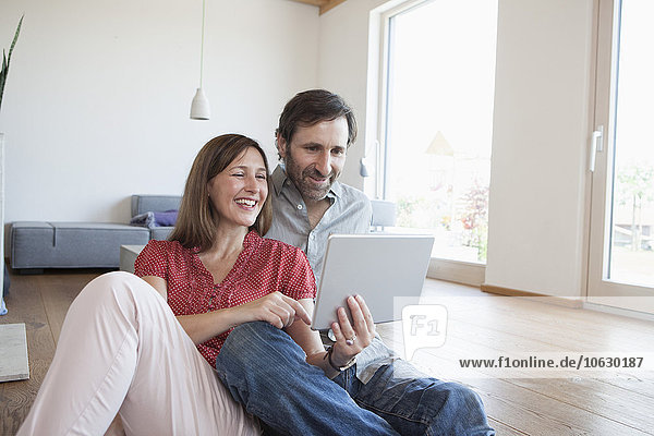 Mature couple sitting on floor  using digital tablet