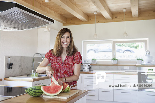 Reife Frau in der Küche schneidet Wassermelone