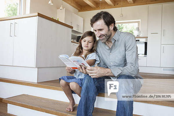 Vater und Tochter sitzen auf Küchenstufen und lesen Buch