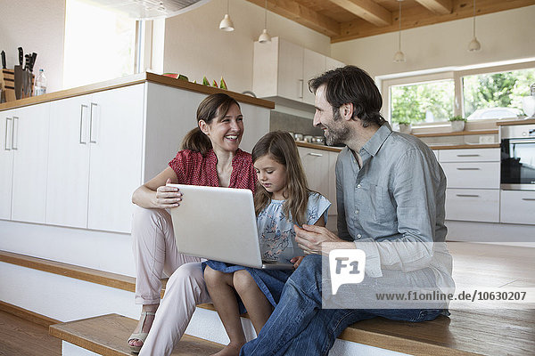 Glückliche Familie sitzend auf Küchenstufen  Tochter mit Laptop