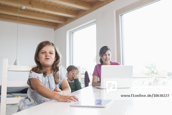 Kleines Mädchen mit digitalem Tablett  Mutter und Bruder mit Laptop im Hintergrund