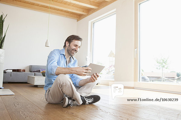 Erwachsener Mann zu Hause mit digitalem Tablett auf dem Boden sitzend