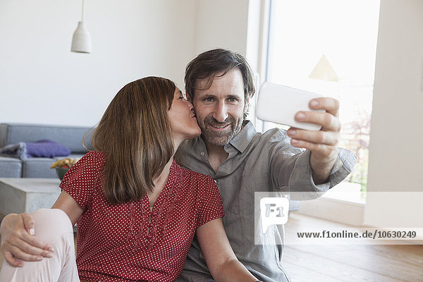 Mature couple sitting on floor taking selfie with smart phone