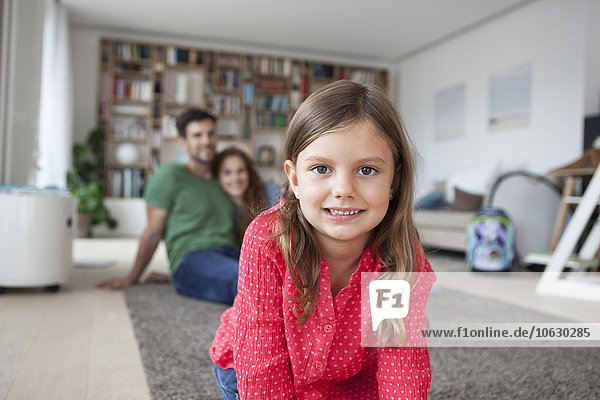 Porträt des lächelnden Mädchens und ihrer Eltern im Hintergrund im Wohnzimmer