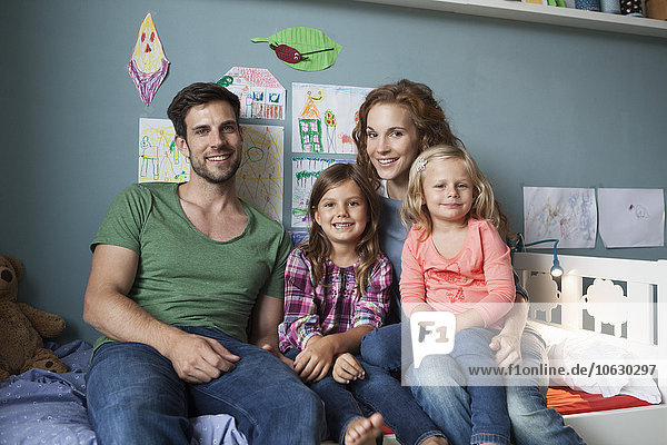 Familienbild eines Paares mit ihren kleinen Töchtern  die zusammen auf dem Bett im Kinderzimmer sitzen.
