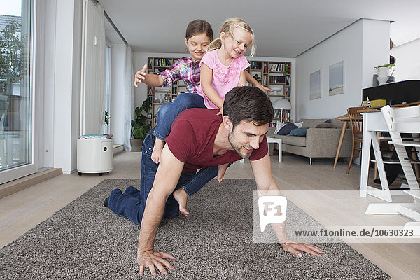 Mann  der mit seinen kleinen Töchtern im Wohnzimmer spielt.