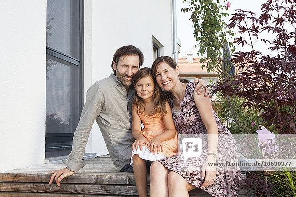 Porträt einer lächelnden Familie mit Tochter auf der Terrasse sitzend