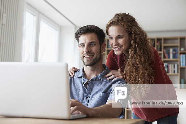 Smiling couple at home looking at laptop