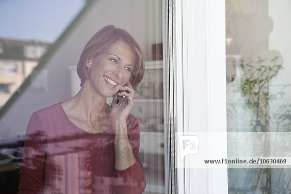 Lächelnde Frau am Telefon am Fenster