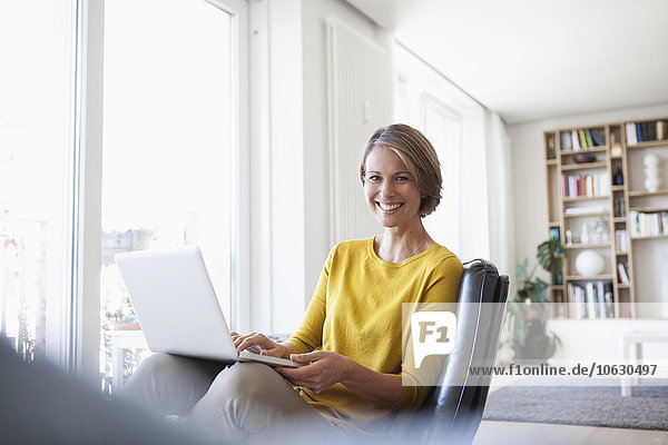 Happy woman at home sitting on leather chair using laptop