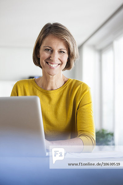 Portrait of smiling woman at home using laptop
