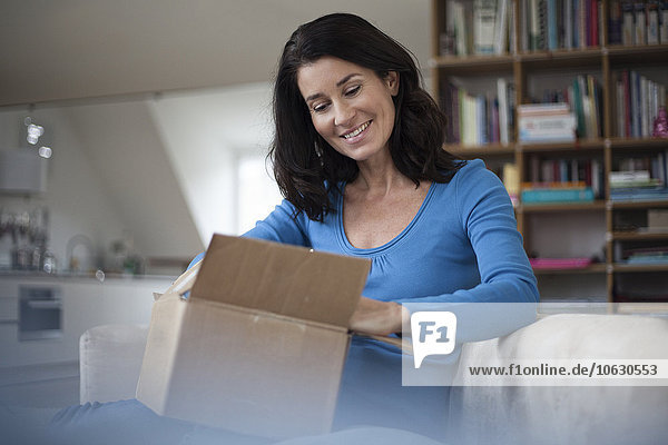 Smiling woman at home sitting on couch unpacking parcel