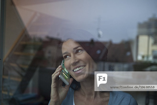 Smiling woman behind windowpane on cell phone