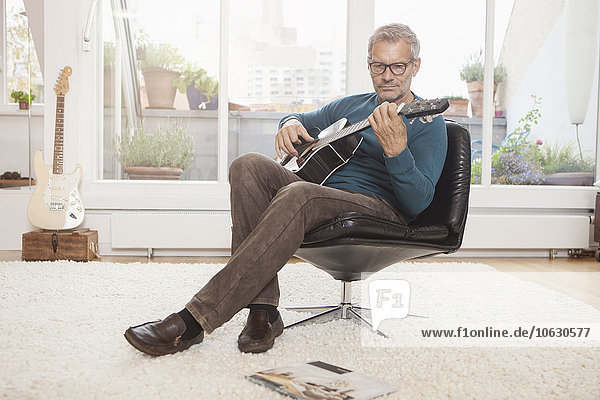Erwachsener Mann zu Hause im Sessel sitzend  Gitarre spielend