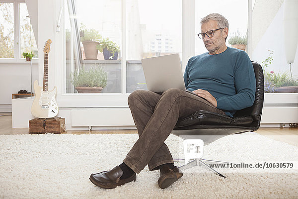 Mature man at home sitting in chair using laptop