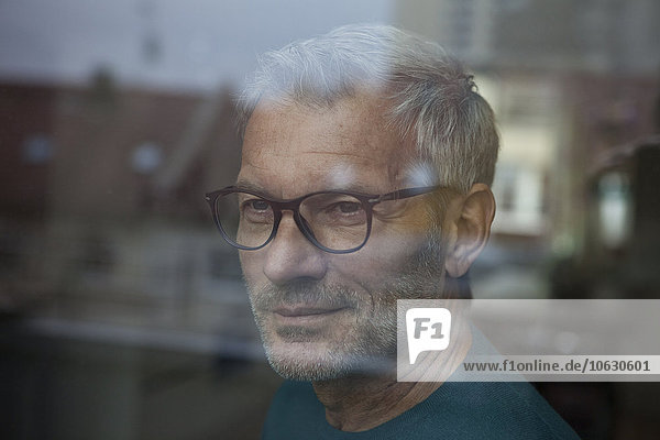 Mature man behind windowpane looking out