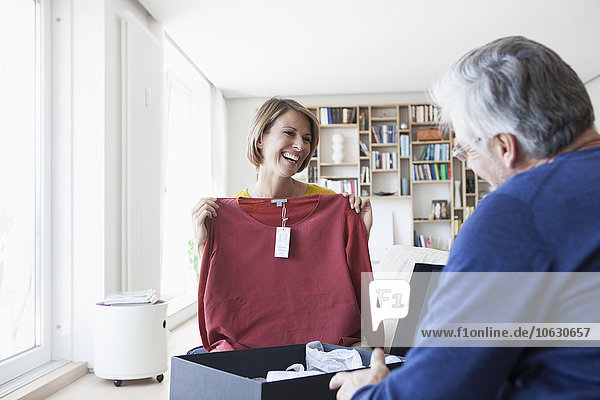 Lächelnde Frau zeigt Ehemann ihren neuen Pullover im Wohnzimmer