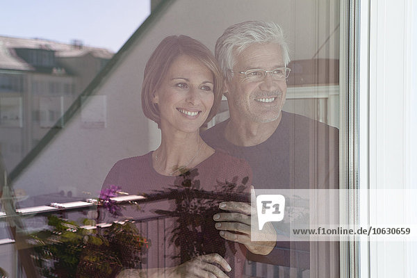 Lächelndes Paar schaut durch die Fensterscheibe