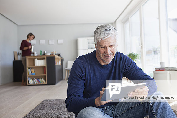 Man sitting on the floor at home using digital tablet