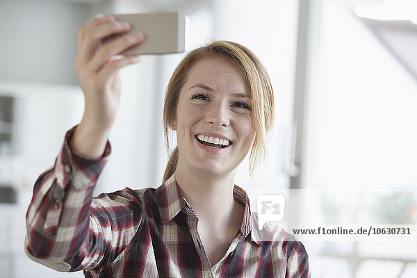 Porträt einer lächelnden jungen Frau  die einen Selfie mit ihrem Smartphone nimmt.