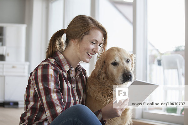 Lächelnde junge Frau sitzt neben ihrem Hund und schaut auf die digitale Tafel.